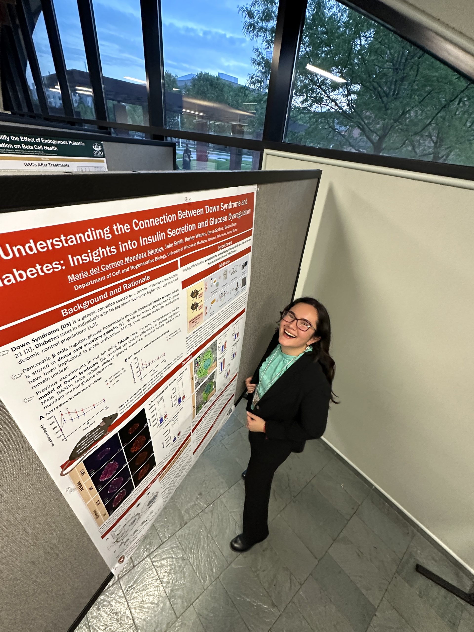Maria standing with her poster at Midwest Islet Club in May, 2025