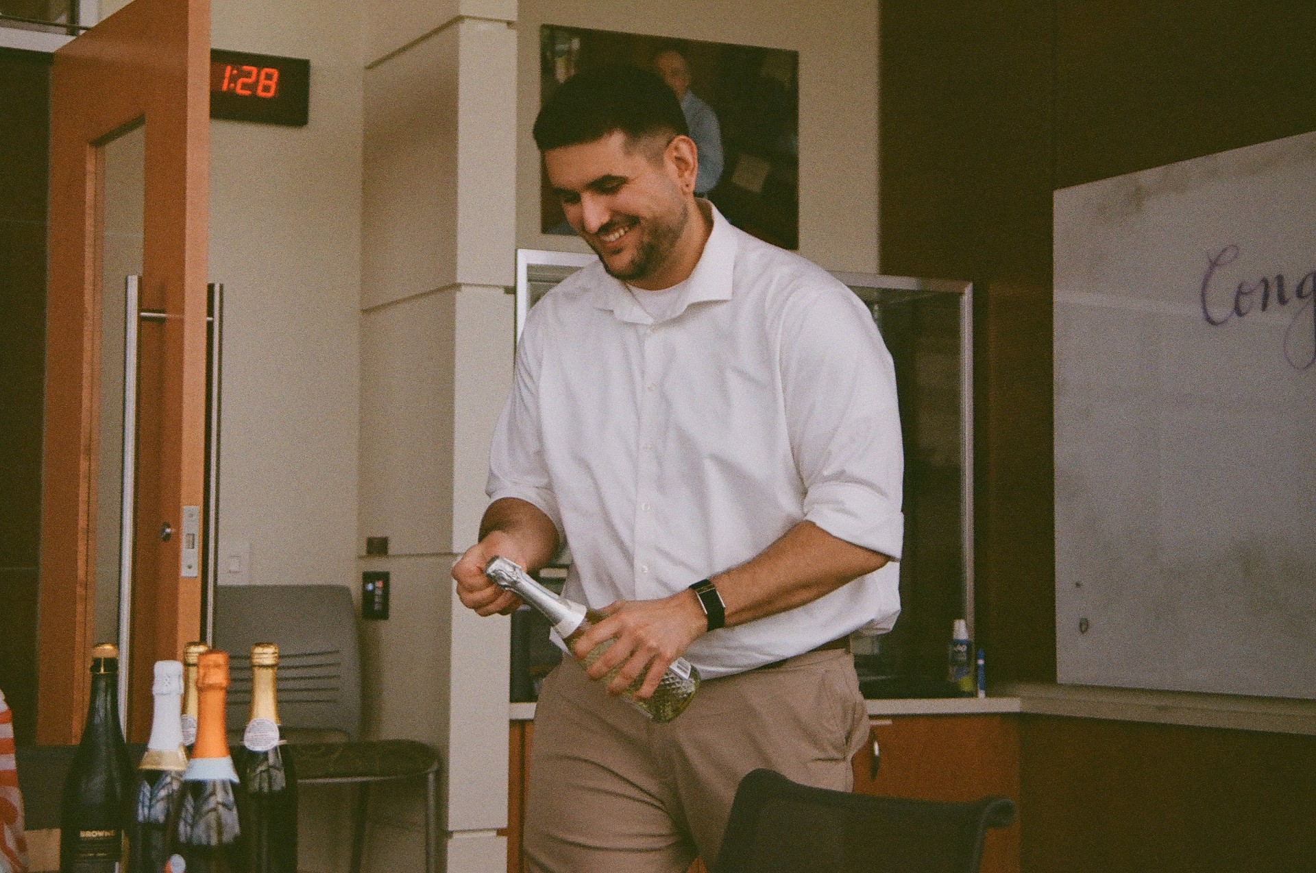 Cyrus opening a bottle of champagne after his defense at approximately 1:28pm in July, 2026